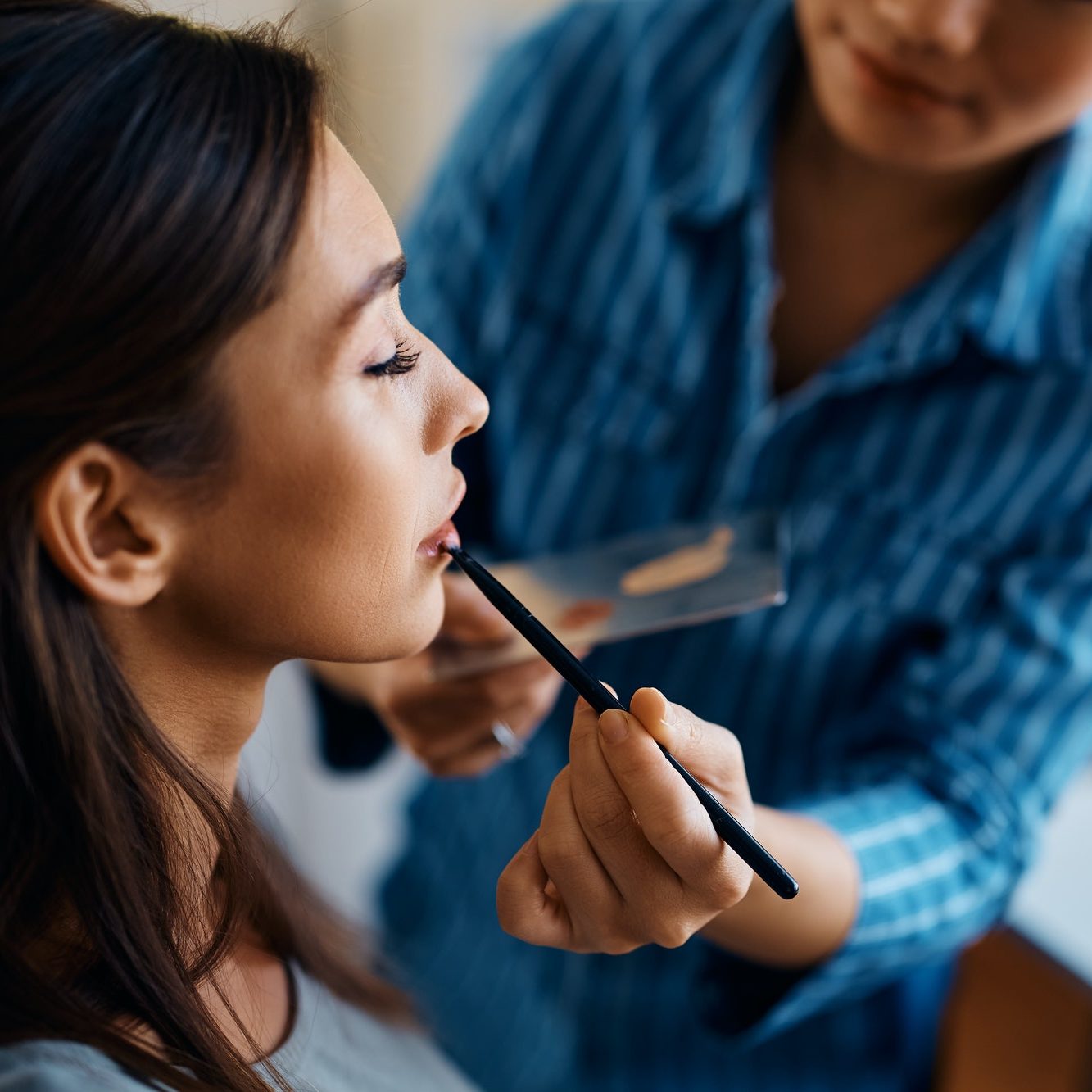Close up of makeup artist applying lipstick with a brush on woman's lips.