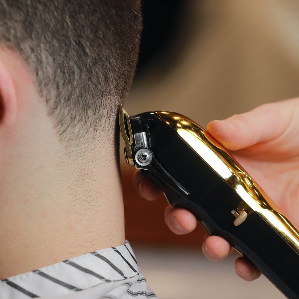 Hairdresser, barber cutting the hair from the back of the client's head with a gold electric clipper