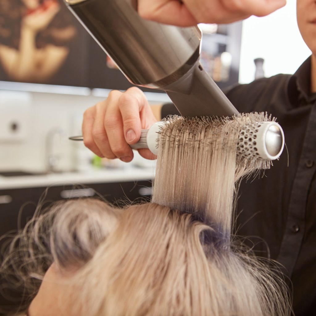 Hairdresser doing blowout hairstyle for client in beauty salon