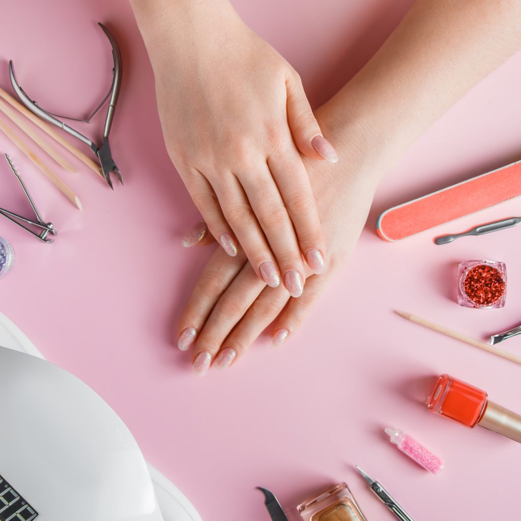 Nail care procedure in a beauty salon. Female hands and tools for manicure on a pink background.