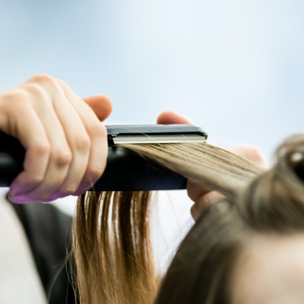 Professional hairdresser straightening long blond hair using straightener