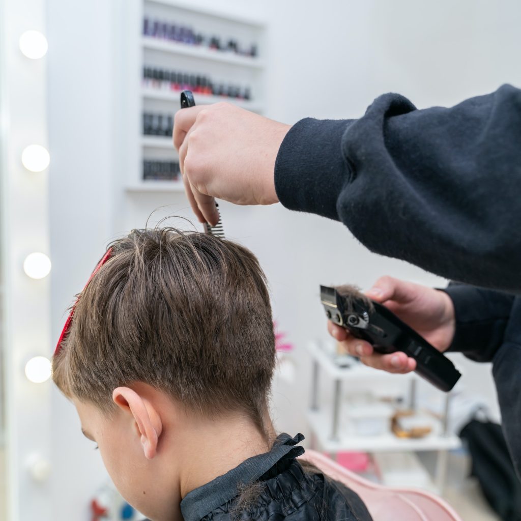 The hairdresser makes a boy's haircut with a clipper